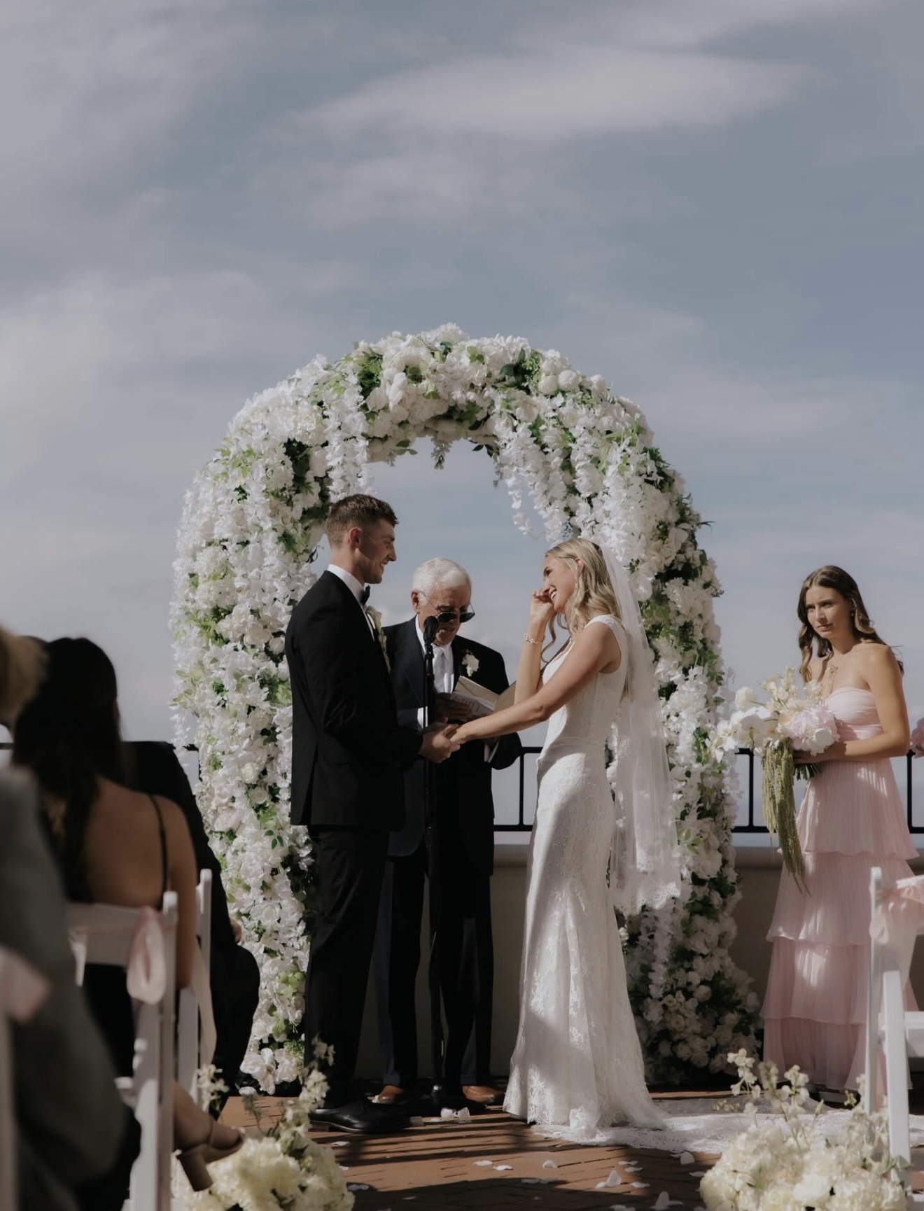 Bride and groom exchanging vows under a white floral arch